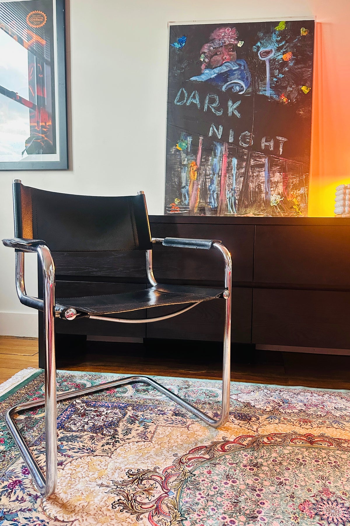 Black chair with chrome legs in a room with a colorful rug and wall art.