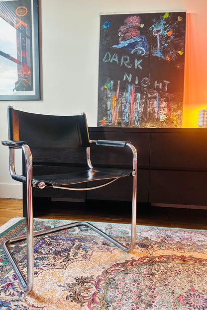 Black chair with chrome legs in a room with a colorful rug and wall art.