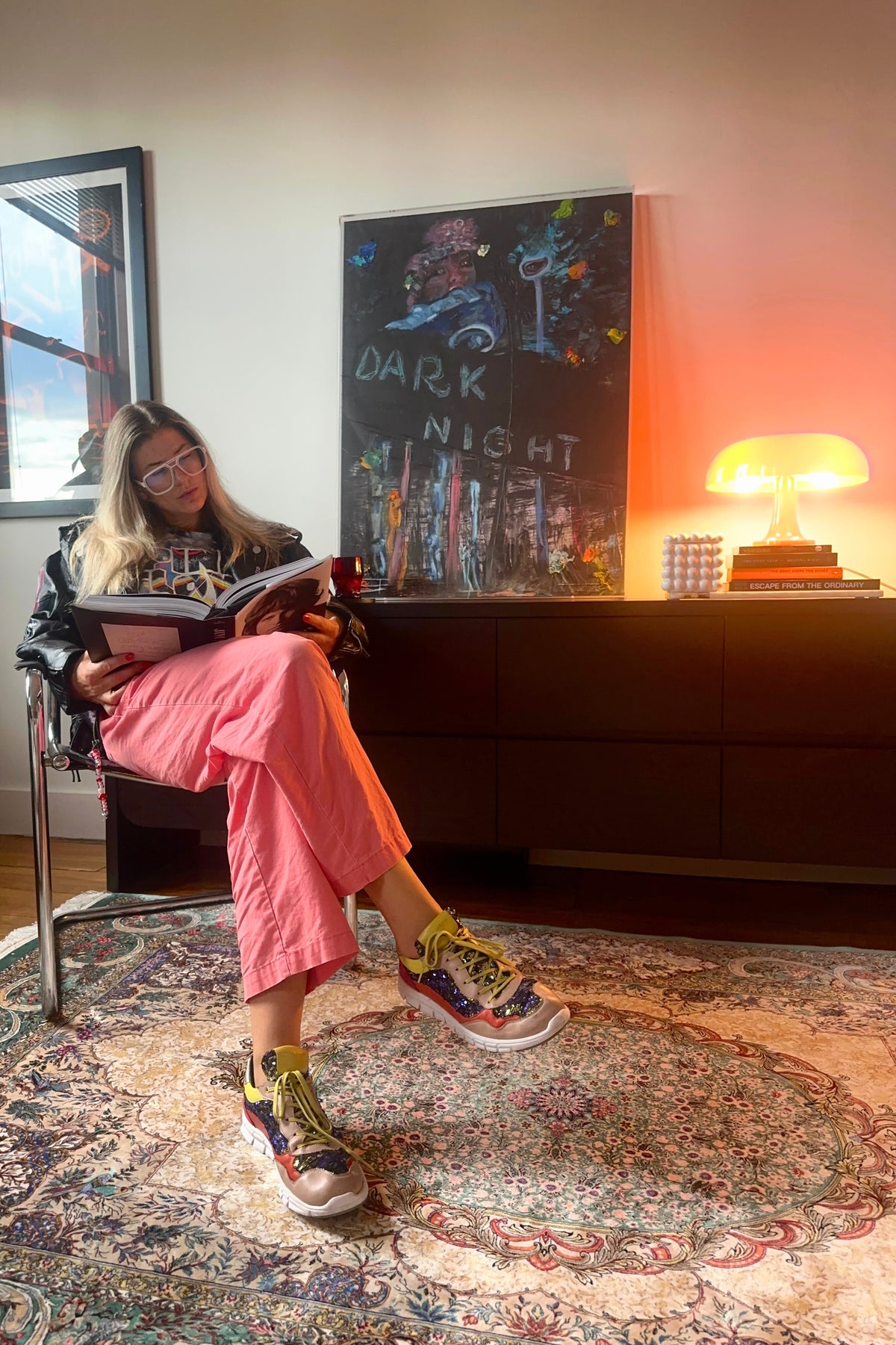 Person sitting on a chair reading a book in a room with a colorful rug and wall art.
