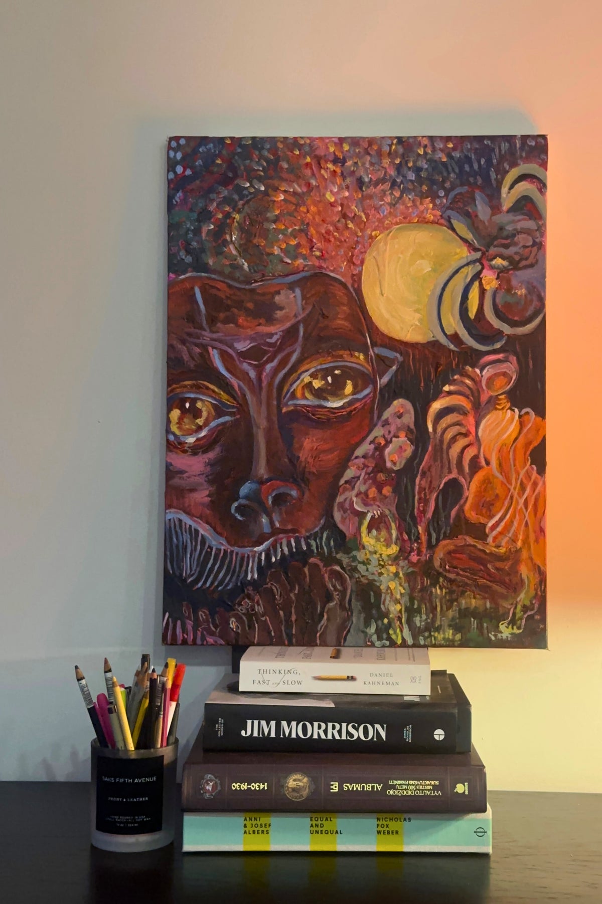 Notebook with a colorful cover featuring a face and flames, placed on books with a pen holder beside it.