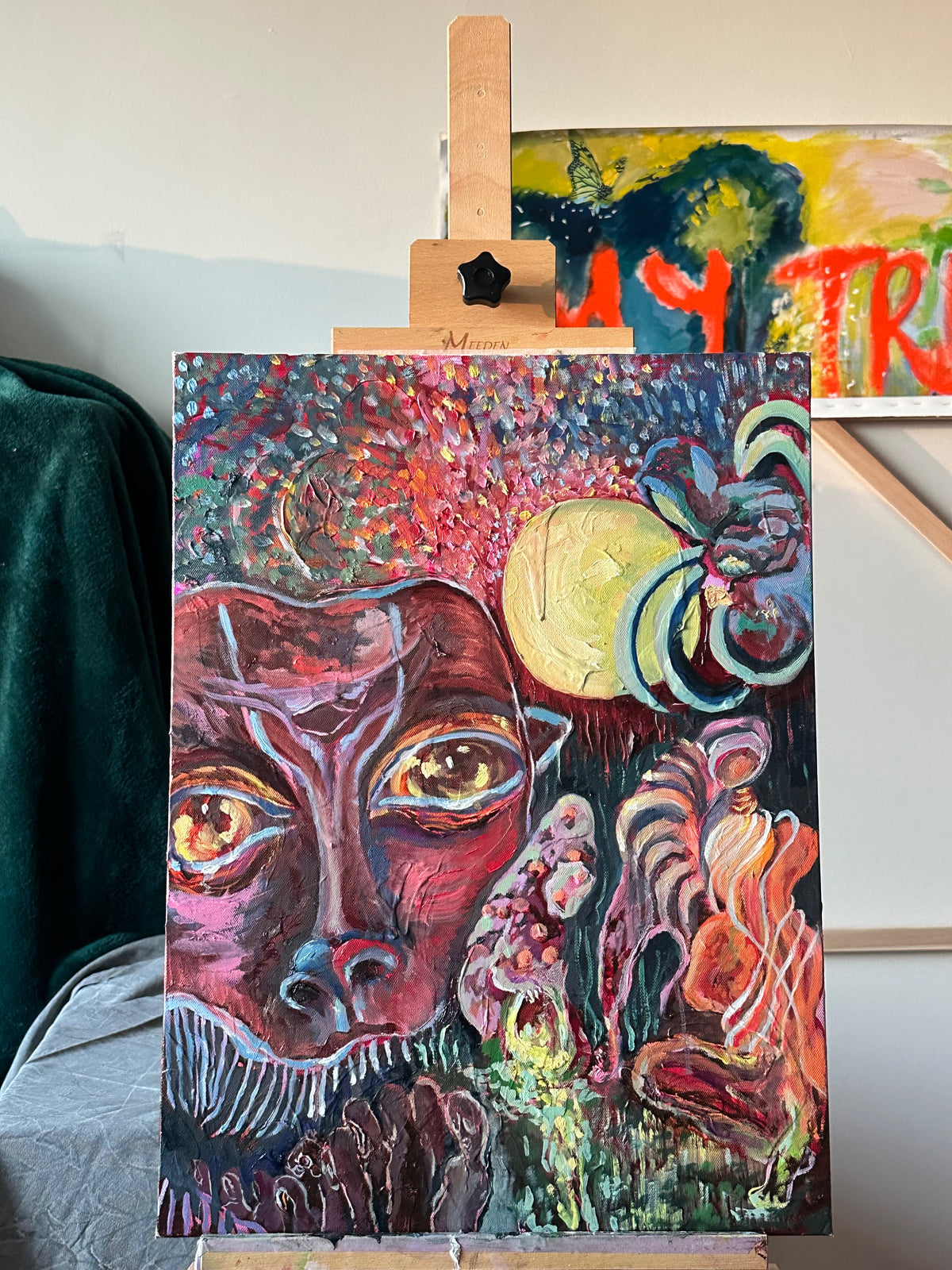 Colorful abstract painting on an easel with another painting in the background.
