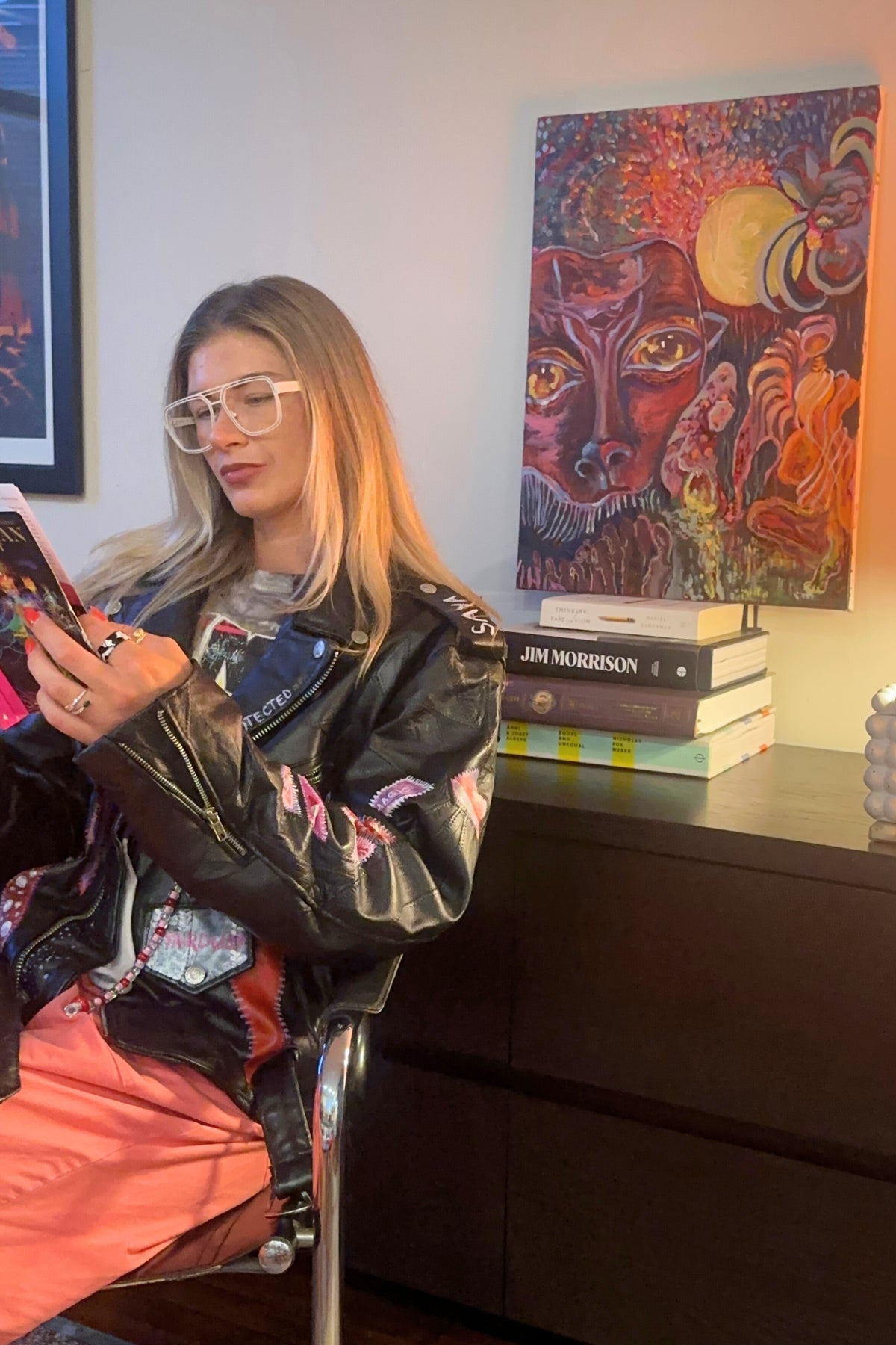 Woman in a stylish jacket holding a phone in a room with a colorful painting on the wall.