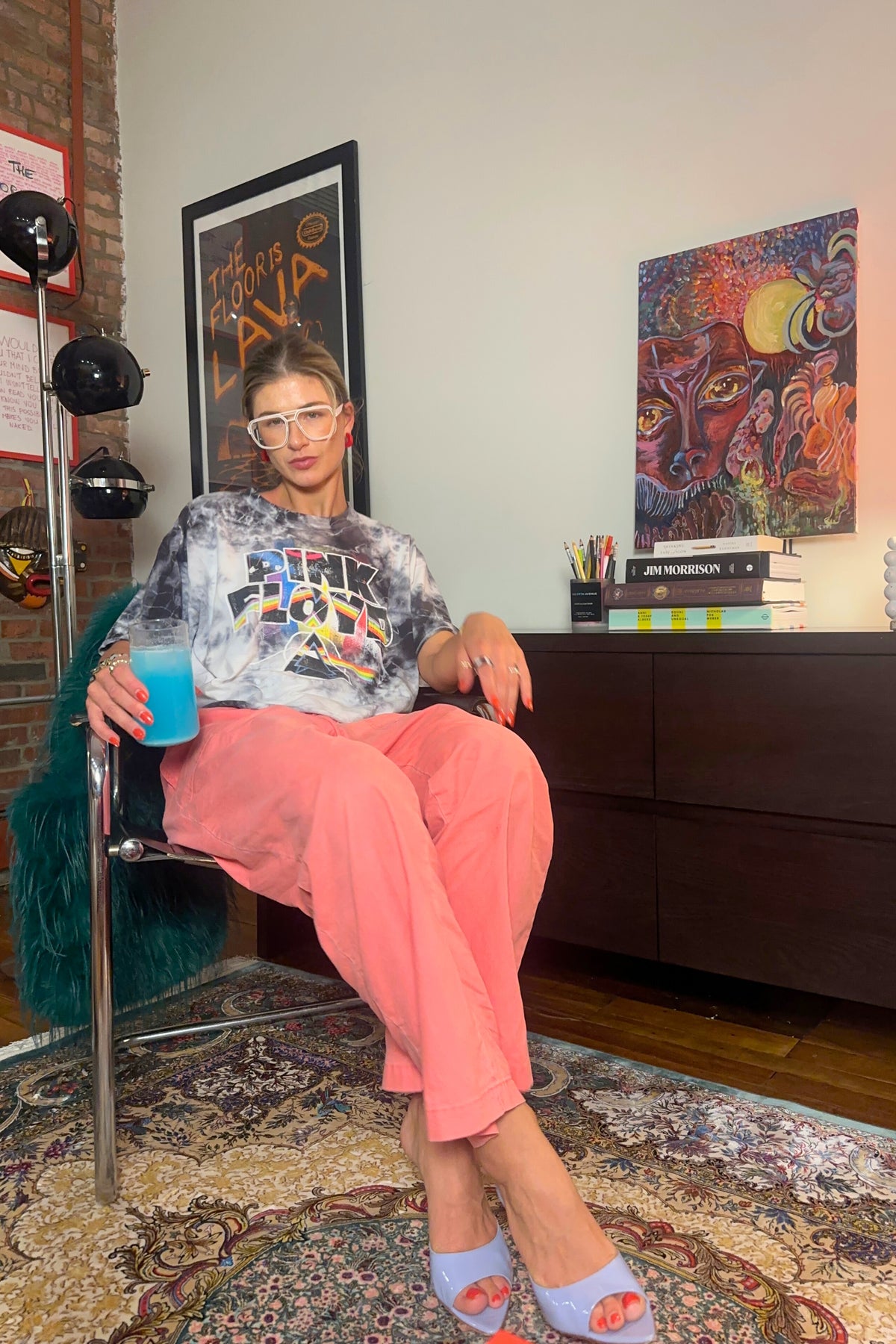 Person sitting in a chair holding a drink in a room with colorful artwork on the walls.