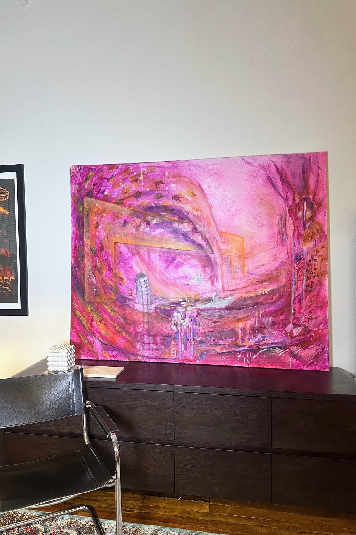 Abstract pink and purple painting on a wall above a dark wooden cabinet.