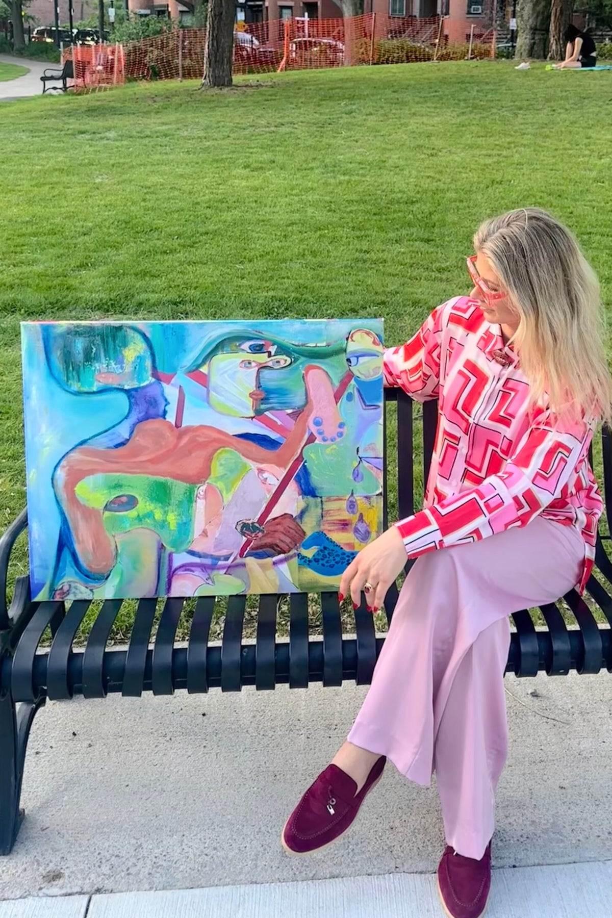 Woman sitting on a park bench with a colorful abstract painting