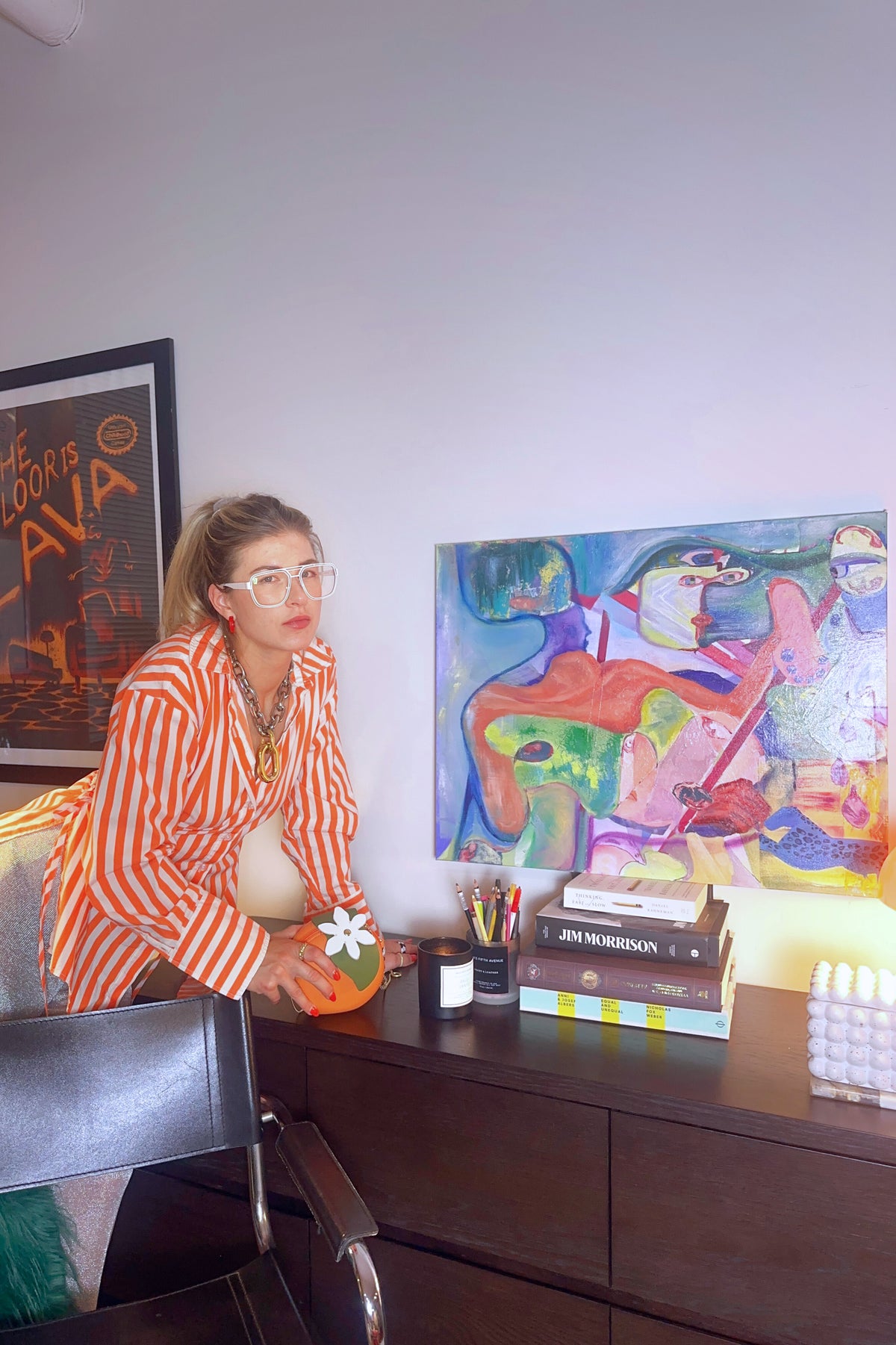 Person in a striped shirt sitting at a desk with a colorful painting on the wall.
